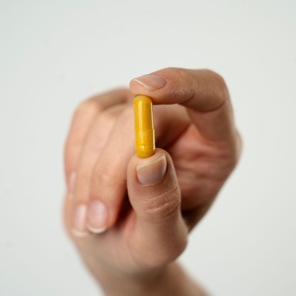 Mână ținând o capsulă portocalie de Colagenus Capsule de la Faunus Plant, pe fundal alb.