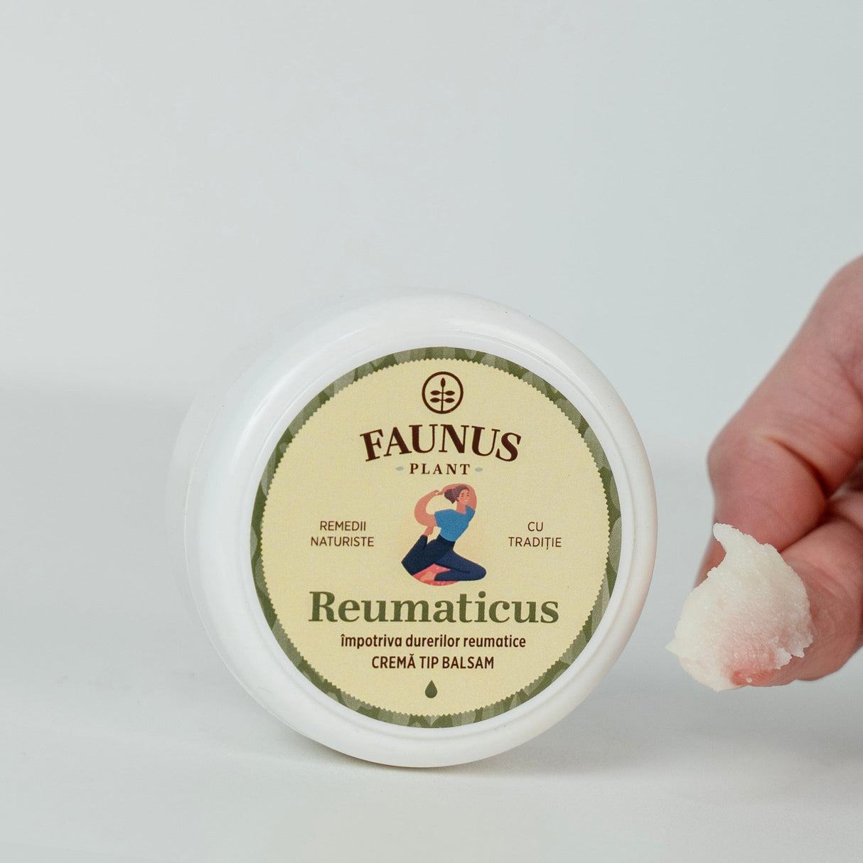 Cremă tip balsam Reumaticus de la Faunus Plant, ambalată într-un recipient alb de 100 ml, alături de o mână care prezintă textura densă și albă a cremei, specifică pentru aplicare locală. Eticheta produsului indică utilizarea împotriva durerilor reumatice, cu accent pe remediile naturiste și tradiția Faunus Plant.